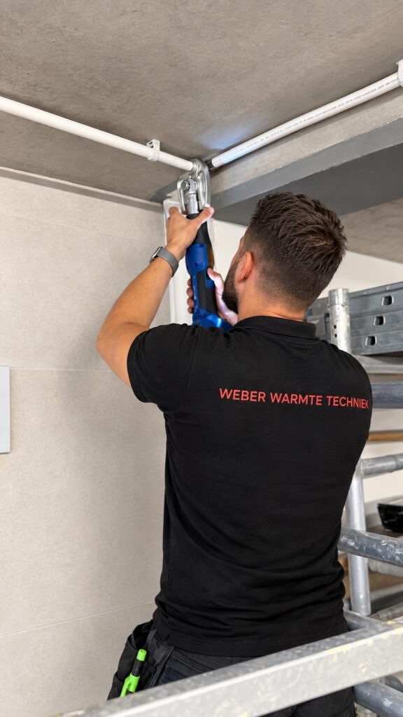 Monteur van Weber Warmtetechniek perst een leiding aan het plafond